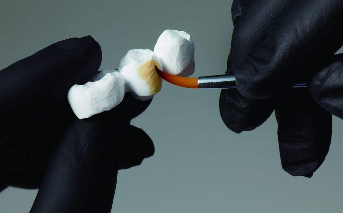 Lab technician staining a zirconia bridge by hand